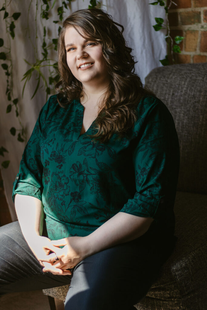 Photo of Brandi in a green floral shirt against a background with plants and brick. The photo is meant to show her creative side and how much she loves nature.